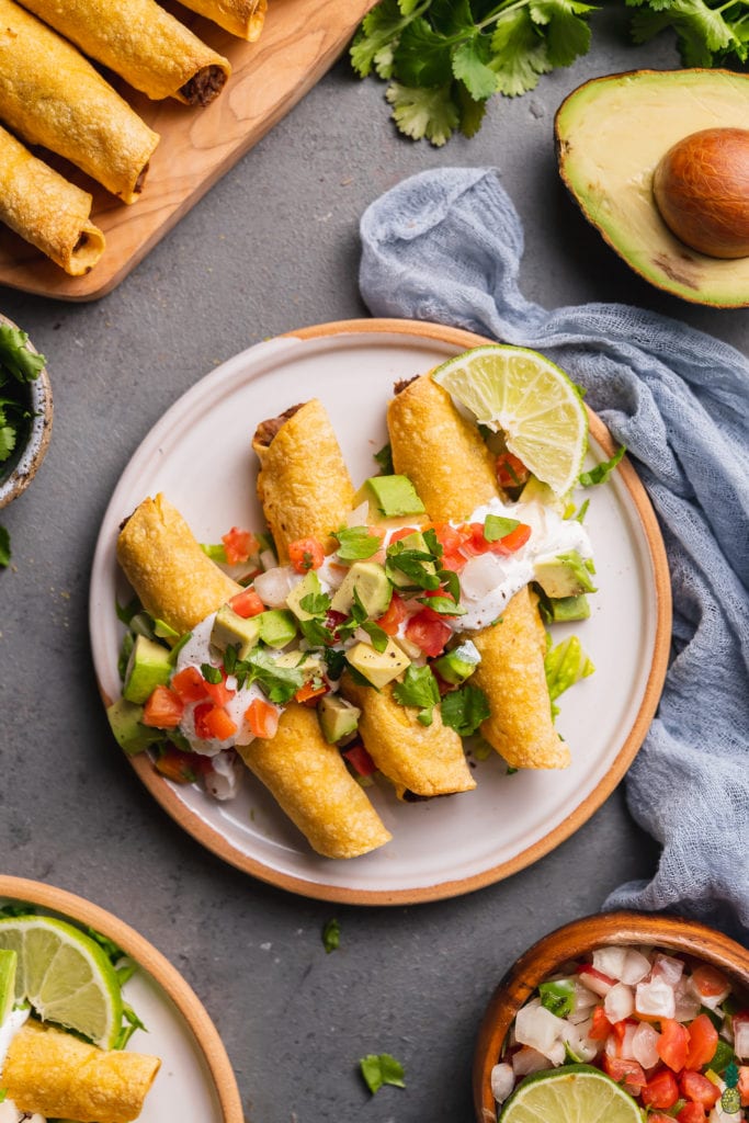 a plate of mushroom potato taquitos with vegan sour cream, pico de gallo, avocado and lime