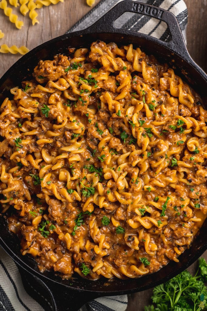 A close up shot of homemade hamburger helper in a cast iron skillet on a wooden backdrop with parsley on top by sweet simple vegan