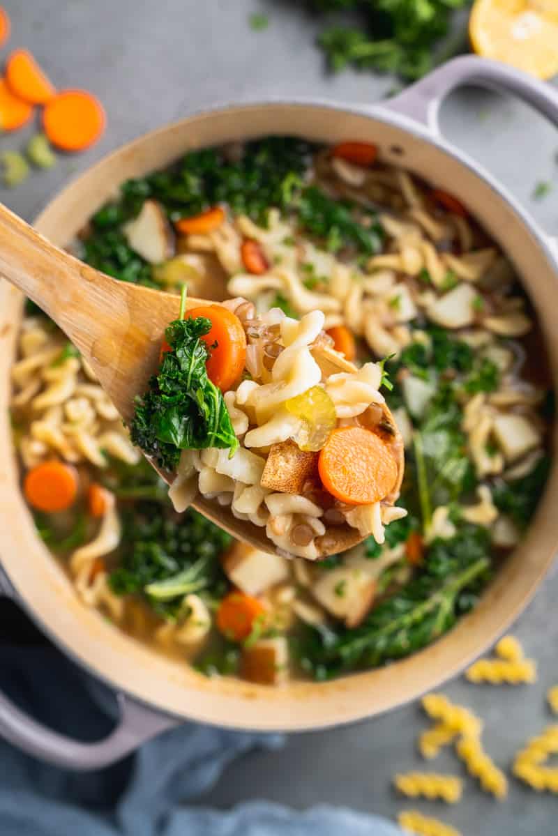 a close up shot of a spoon scooping vegetable noodle soup in a pot