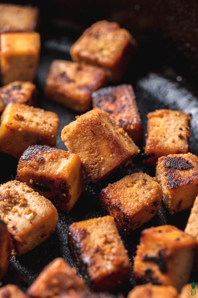 macro image of sesame ginger tofu cubes in cast iron skillet shot at 3/4 angle. 