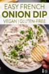 vegan french onion dip in a gray bowl covered in parsley with a potato chip dipped into it for pinterest