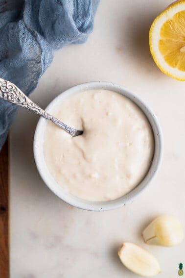 A bowl of homemade garlic aioli with a spoon by sweet simple vegan