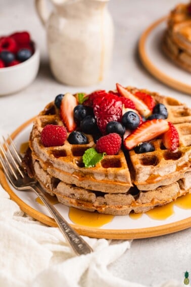 Macro image of vegan rye waffles topped with fruit and smothered with maple syrup.
