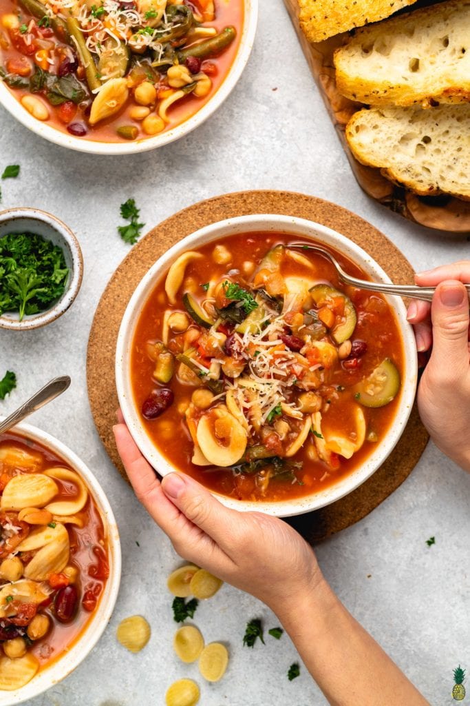 overhead image of bowls of one-pot minestrone soup styled shot from overhead with hands holding bowl