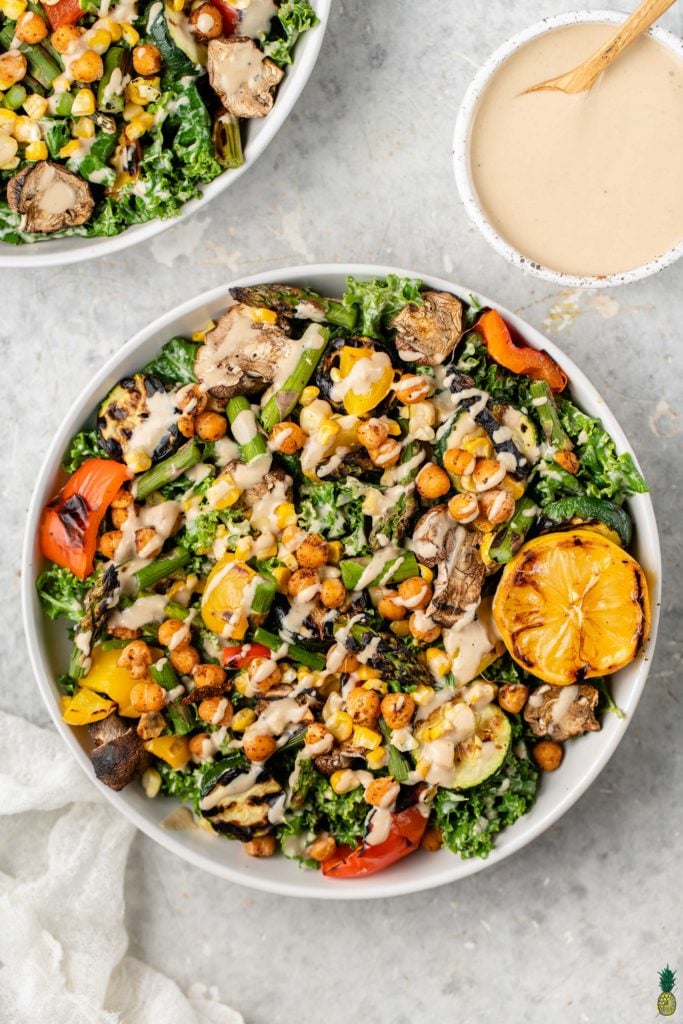 Tahini dressing on a roasted vegetable and chickpea salad in a white bowl by sweet simple vegan