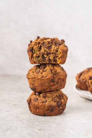 stacked chocolate chip zucchini muffins with a bite taken out of top one