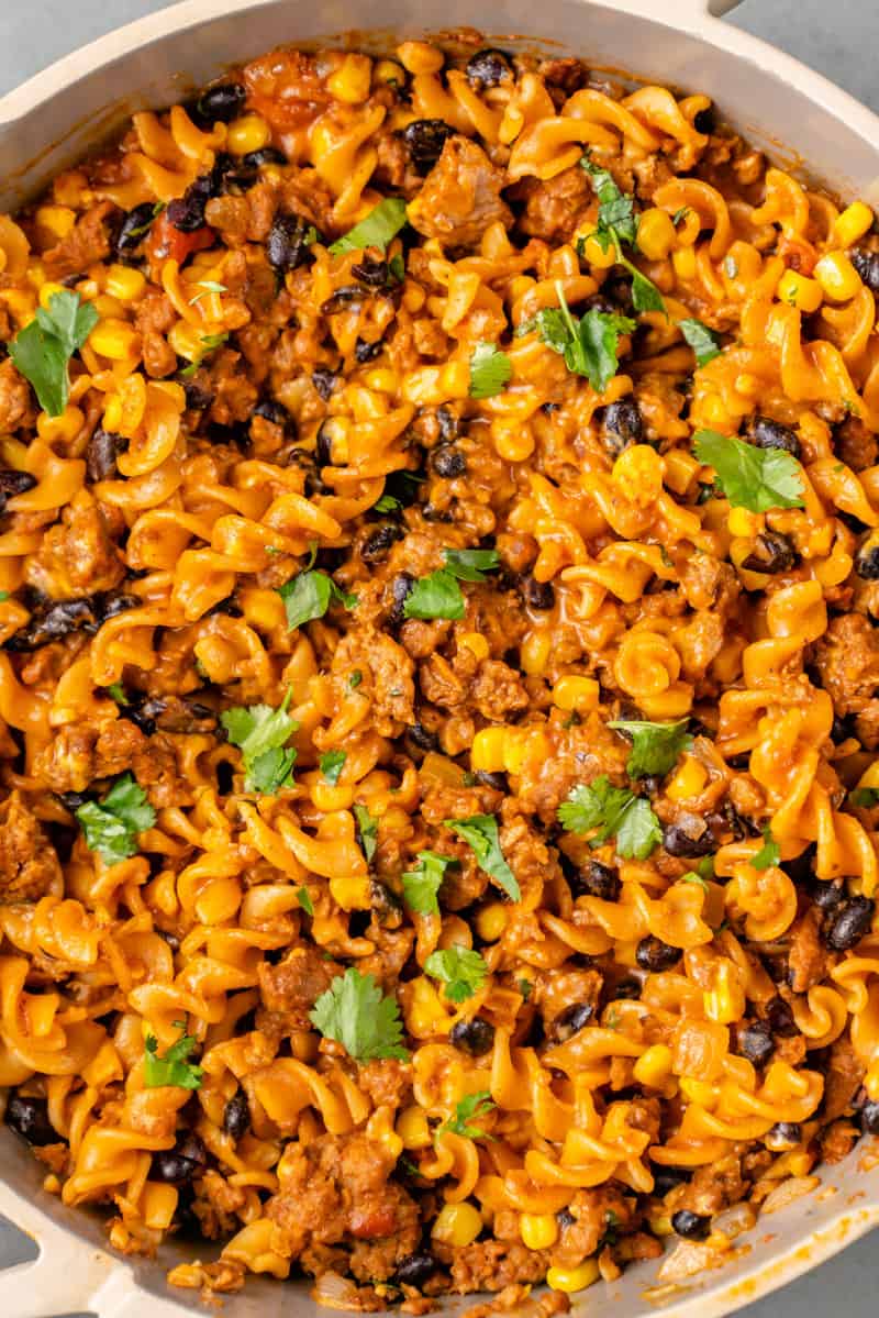 close up shot of creamy vegan taco pasta in a beige pan with cilantro on top by sweet simple vegan