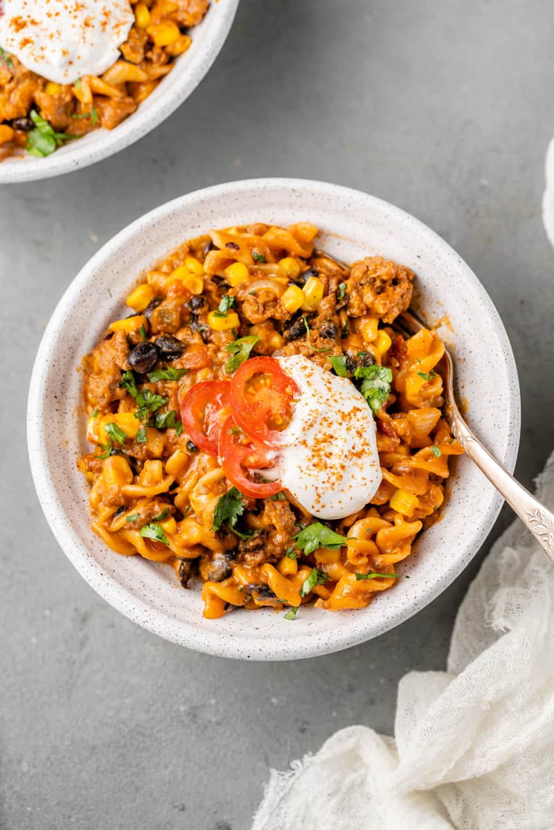 a white bowl of creamy vegan taco pasta and sour cream and tomatoes on top by sweet simple vegan