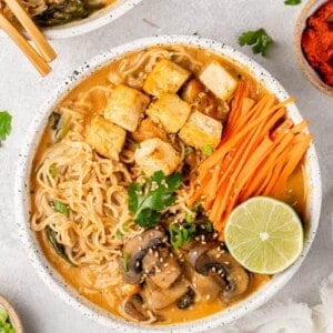 a white bowl of one pot red curry ramen on a gray board by sweetsimplevegan