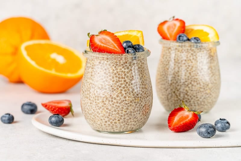 horizontal image of orange creamsicle chia pudding in glass jars topped with fruit. 