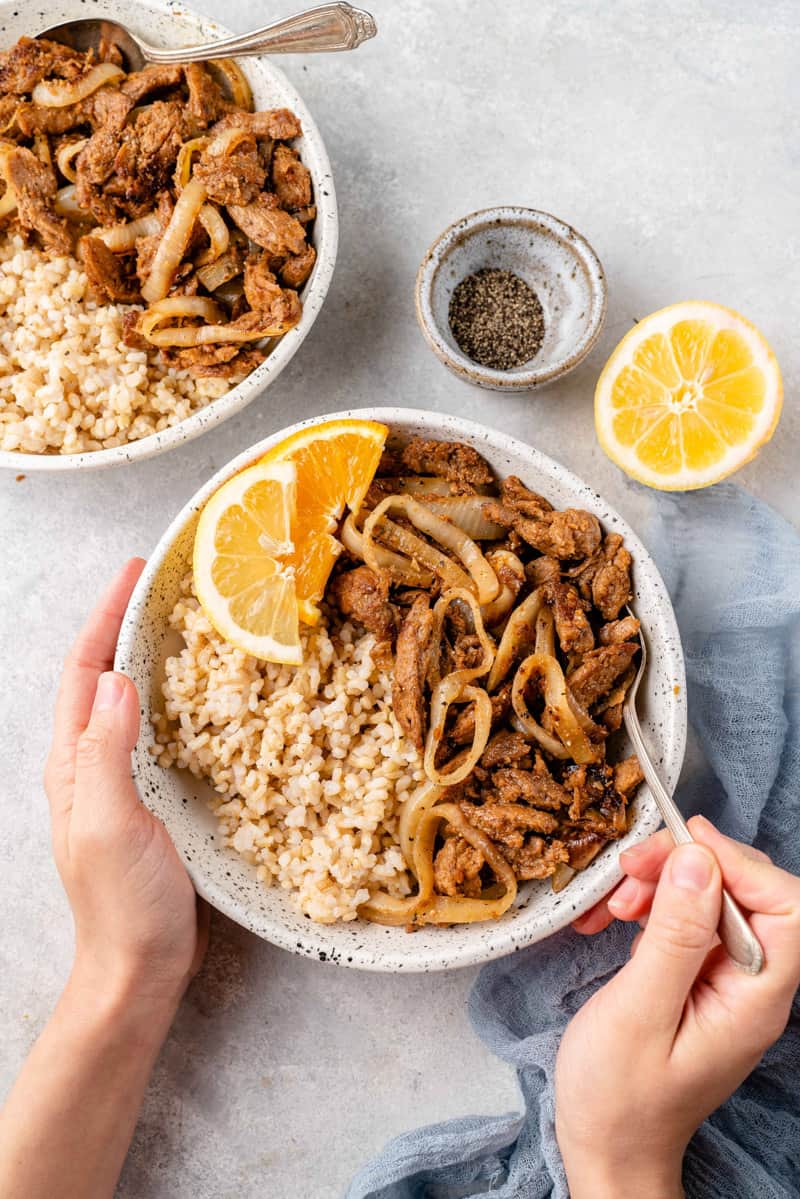 A bowl of bistek tagalog aka filipino beefsteak with rice and onions held with hands and fork inside