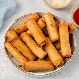 shot of Filipino Lumiang Shanghai in a white bowl with dipping sauces by sweet simple vegan