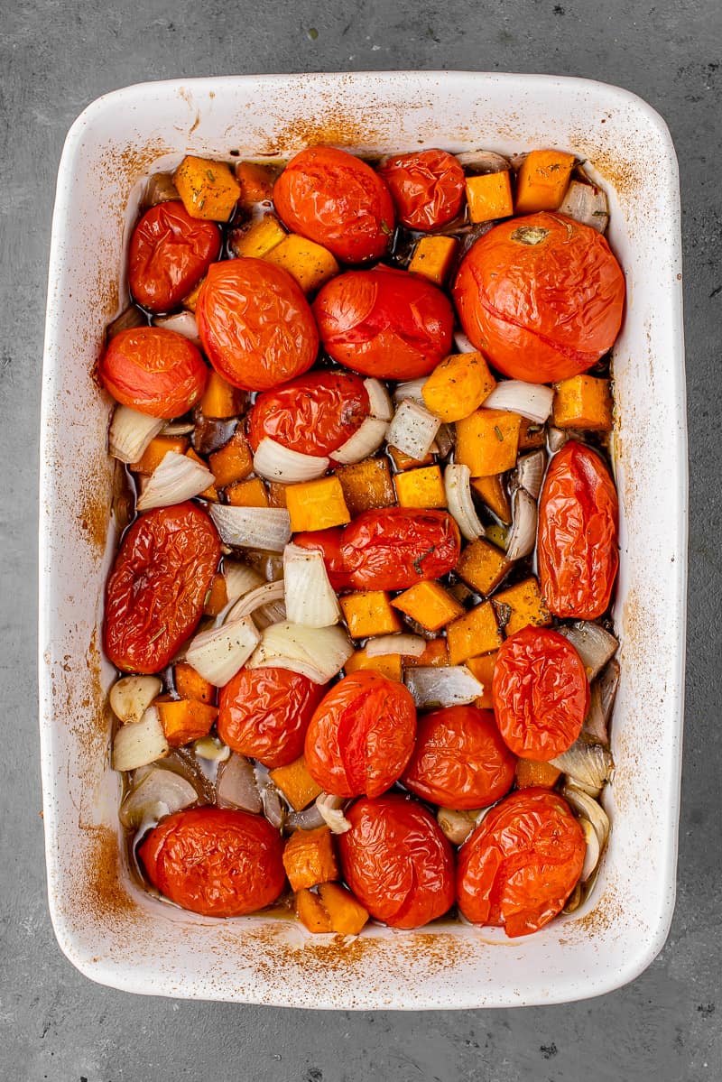 a white casserole dish with roasted butternut squash, tomatoes, garlic, onions herbs, and red wine