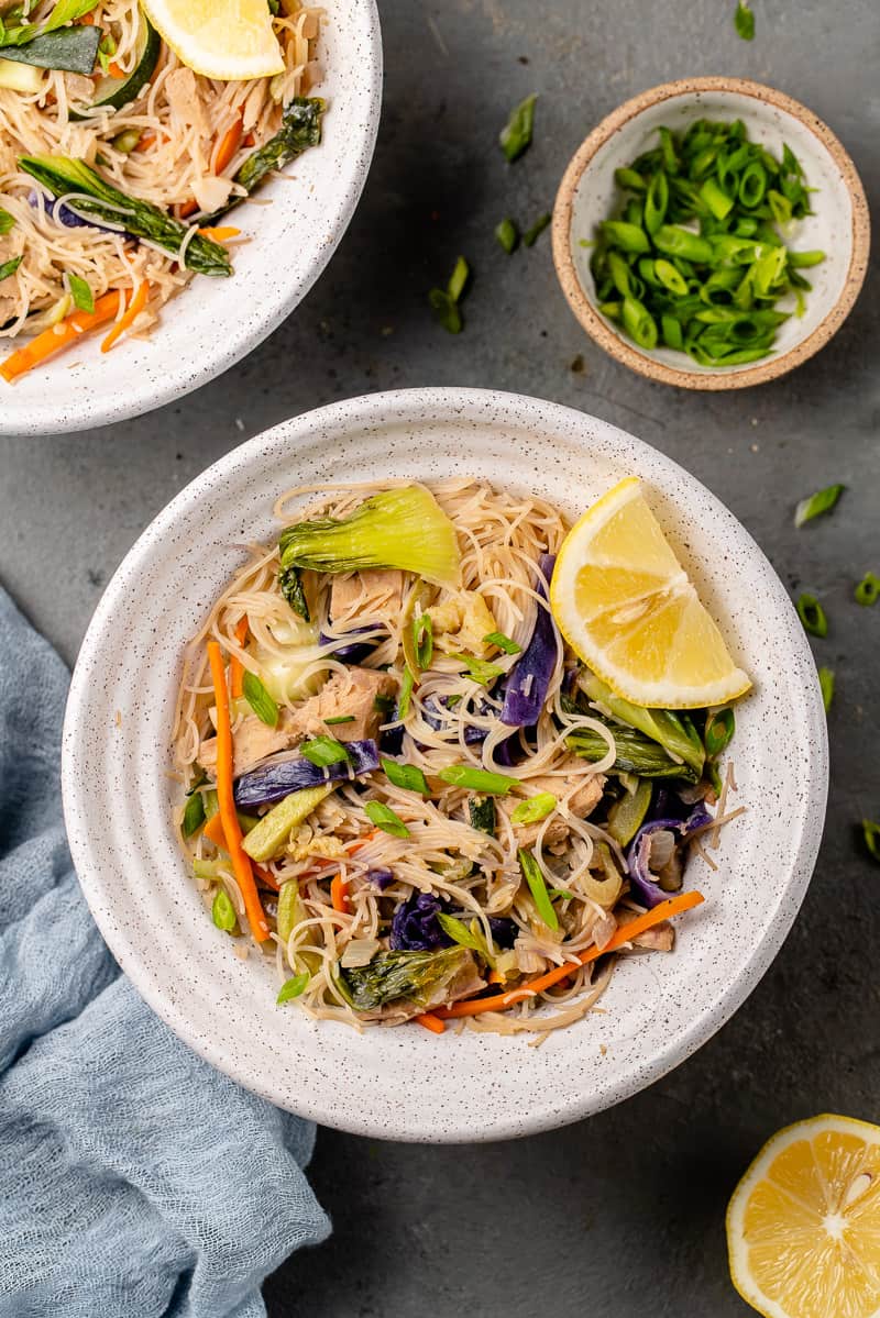 overhead image of bowl of pancit with lemon wedge and green onions on the side