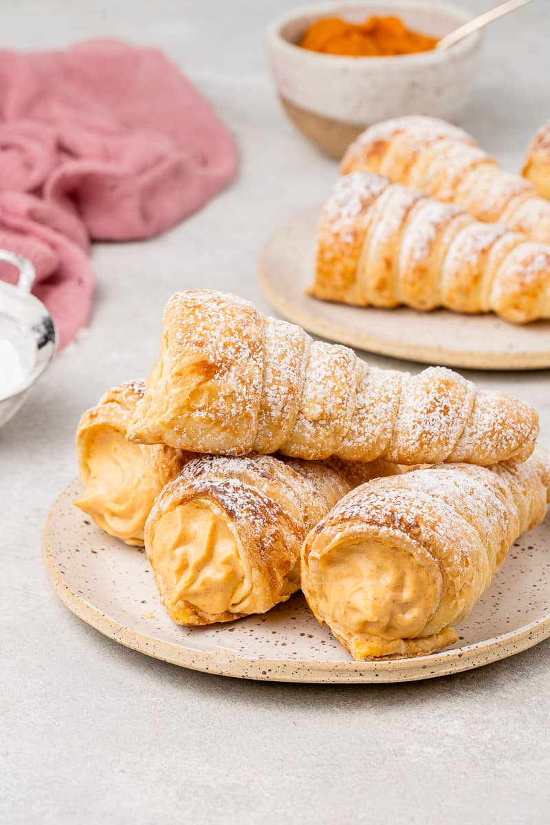 a stack of pumpkin cream horns on a white plate with a pink towel