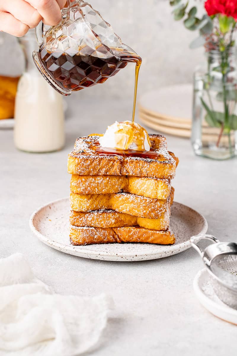 pouring maple syrup on a stack of french toast with whipped cream