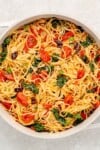 vegan pasta in a pot with tomatoes, kale, olives, basil and parmesan