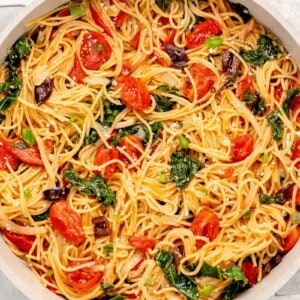 vegan pasta in a pot with tomatoes, kale, olives, basil and parmesan