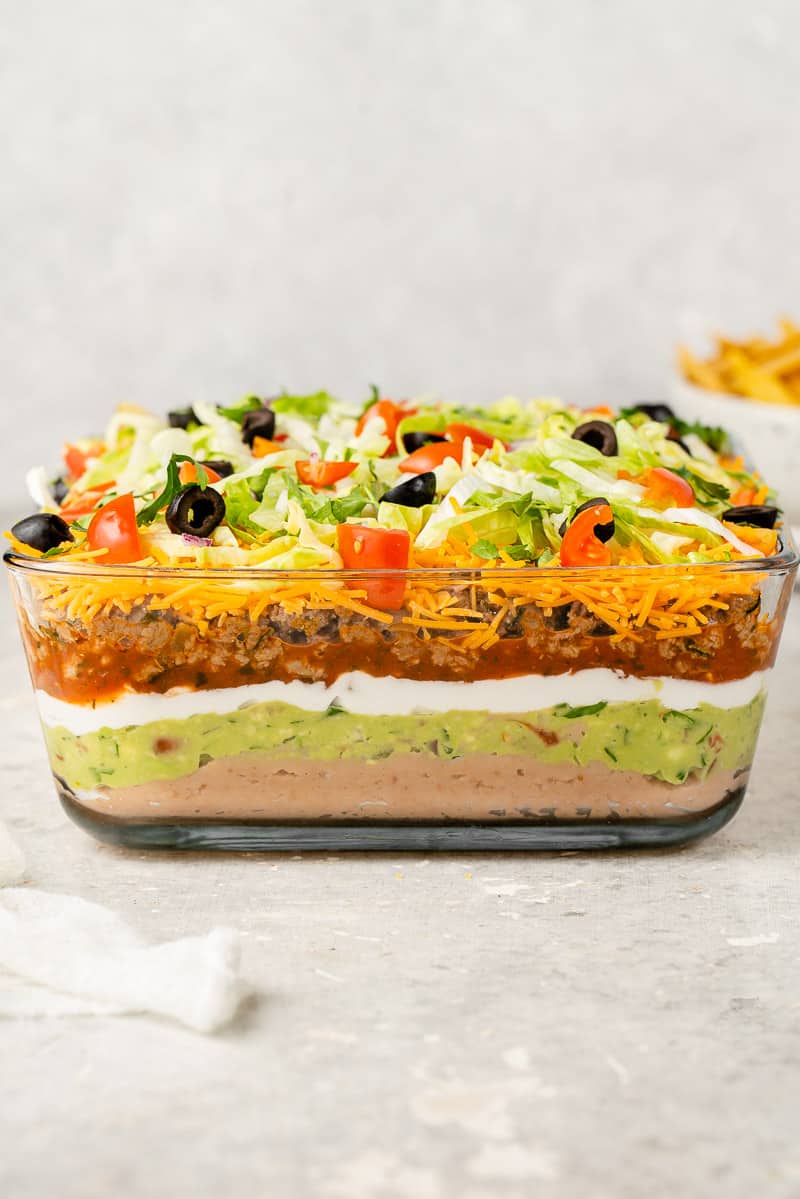 side shot of vegan 7 layer dip in a glass pyrex dish with chips in a bowl and white towel
