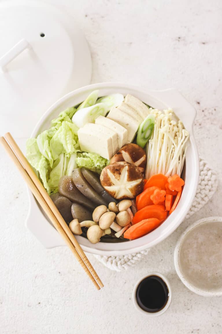 vegetable hot pot in a white bowl on white background with chopsticks and soy sauce. 