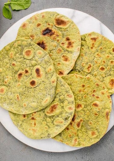 close up of whole wheat spinach tortillas on a marble board surrounded by ingredients