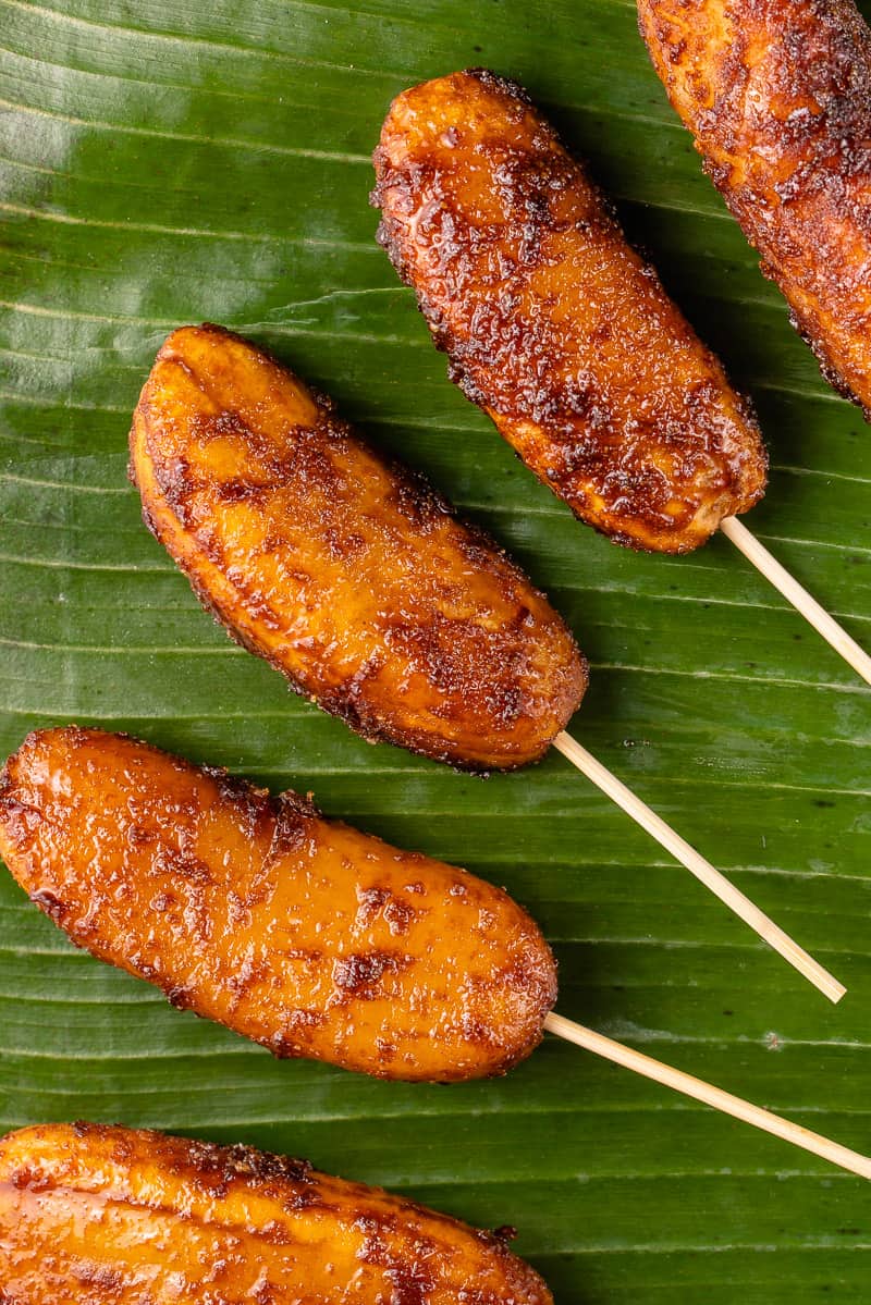a photo of caramelized bananas on barbecue sticks laying on a banana leaf