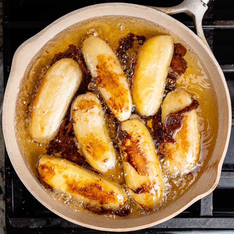 a photo of saba bananas frying in brown sugar in oil in a beige pan