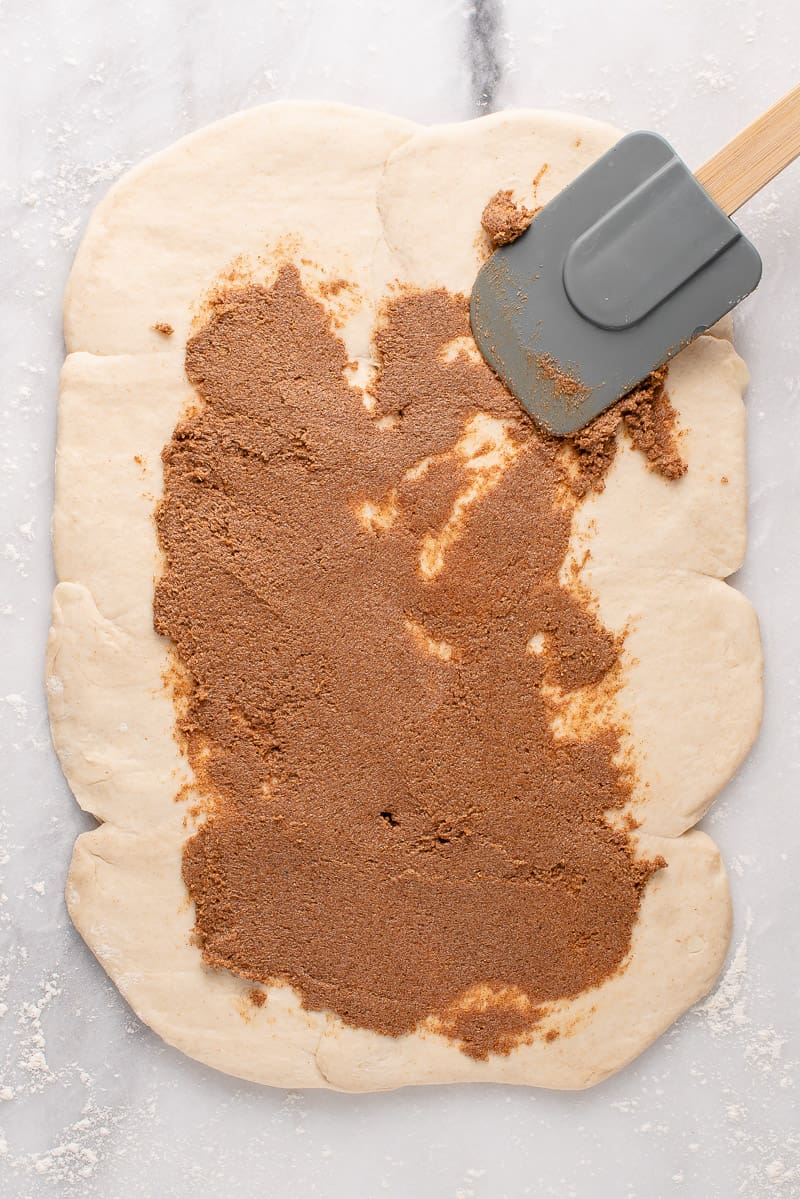 cinnamon sugar filling being spread over uncooked biscuit dough