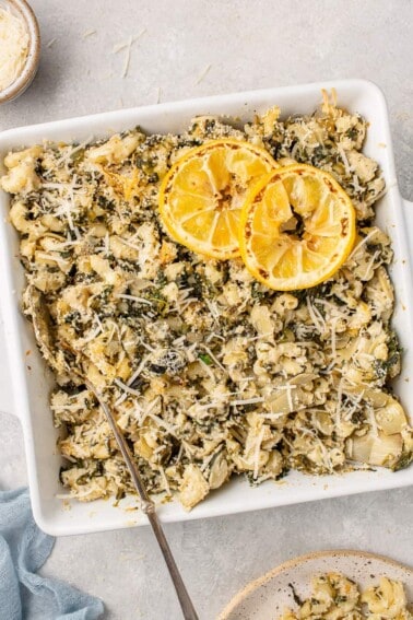 Overhead image of baked spinach artichoke mac and cheese in baking dish with spoon.