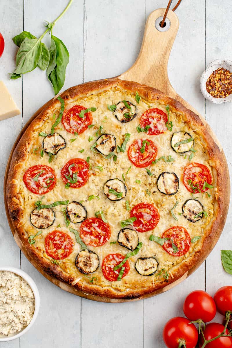 overhead image of white pizza with zucchini and tomatoes on styled background