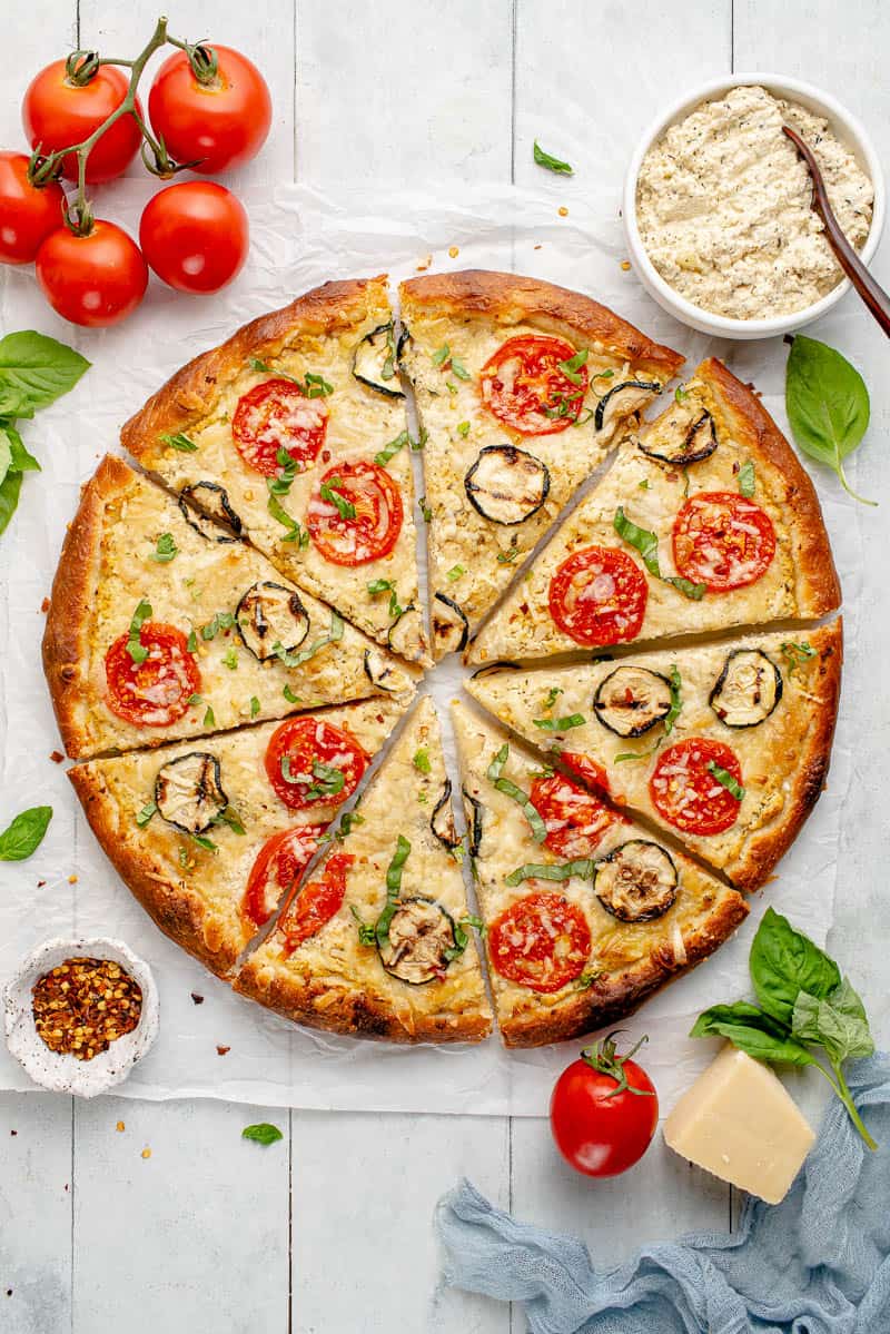 overhead image of white pizza with zucchini and tomatoes with slices separated on styled background