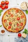 overhead image of white pizza with zucchini and tomatoes on styled background