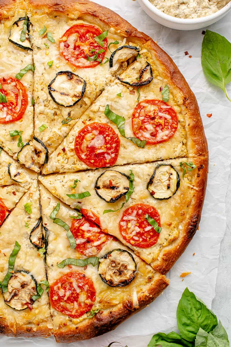 macro image of half white pizza surrounded by basil and cheese