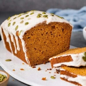 sliced vegan pumpkin bread with cream cheese icing and pumpkin seeds on white board