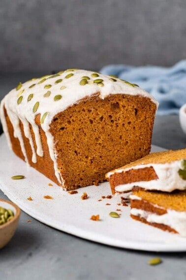 sliced vegan pumpkin bread with cream cheese icing and pumpkin seeds on white board