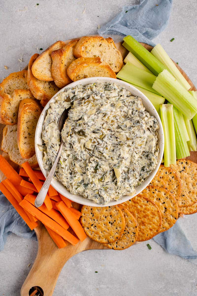 spinach artichoke dip in bowl with crackers and vegetables