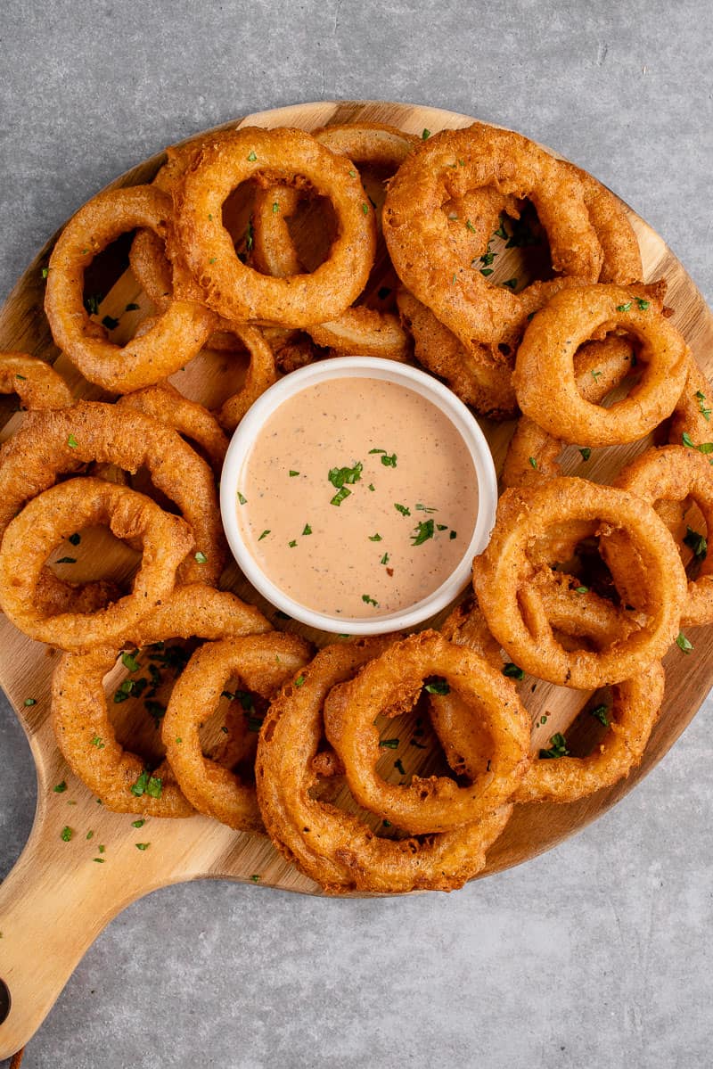 overhead shot of vegan onion rings on a platter with dipping sauce
