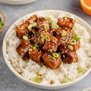 close up of saucy vegan orange tofu in a bowl with rice
