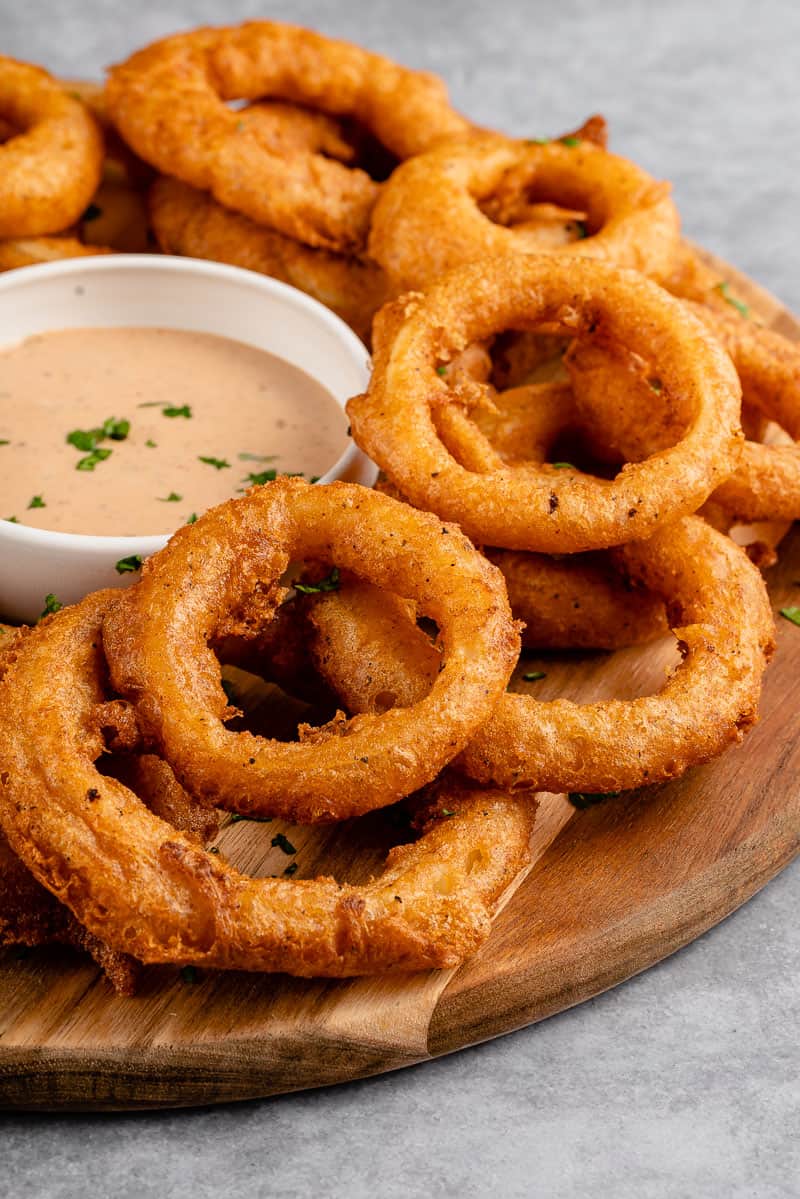 close up shot of vegan onion rings on a platter with dipping sauce