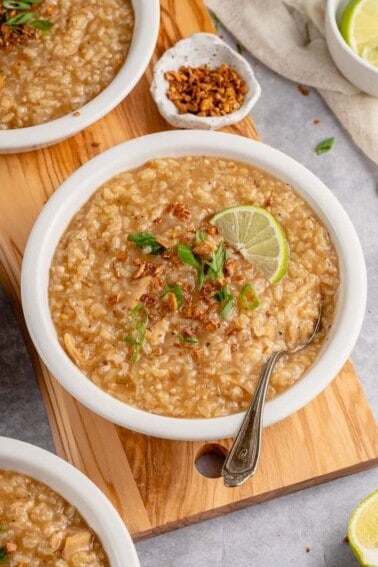 vegan arroz caldo in a white bowl with green onions, lime and crispy garlic
