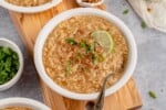 horizontal photo of vegan arroz caldo in a white bowl with green onions, lime and crispy garlic