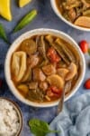 vertical photo of vegan sinigang in a white bowl with a spoon