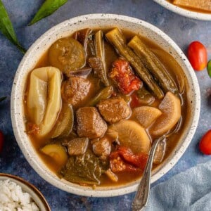 vertical photo of vegan sinigang in a white bowl with a spoon
