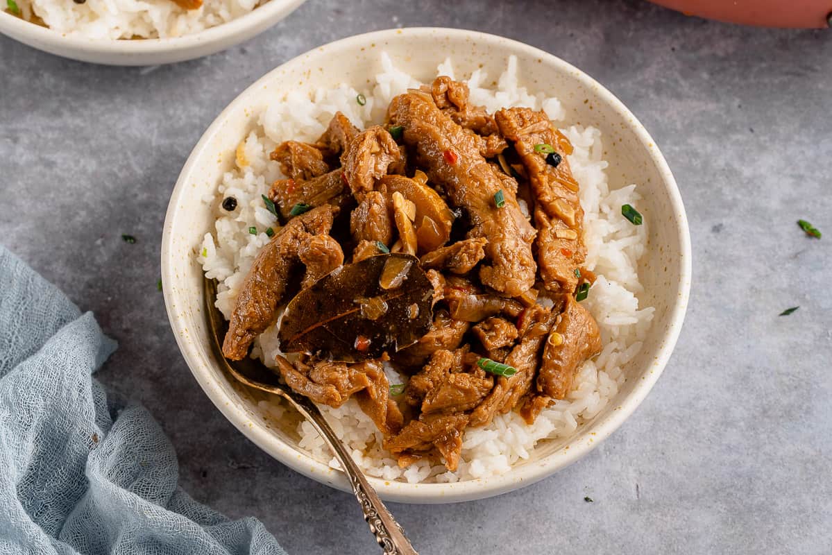 horizontal photo of vegan coconut milk adobo with rice in white bowl