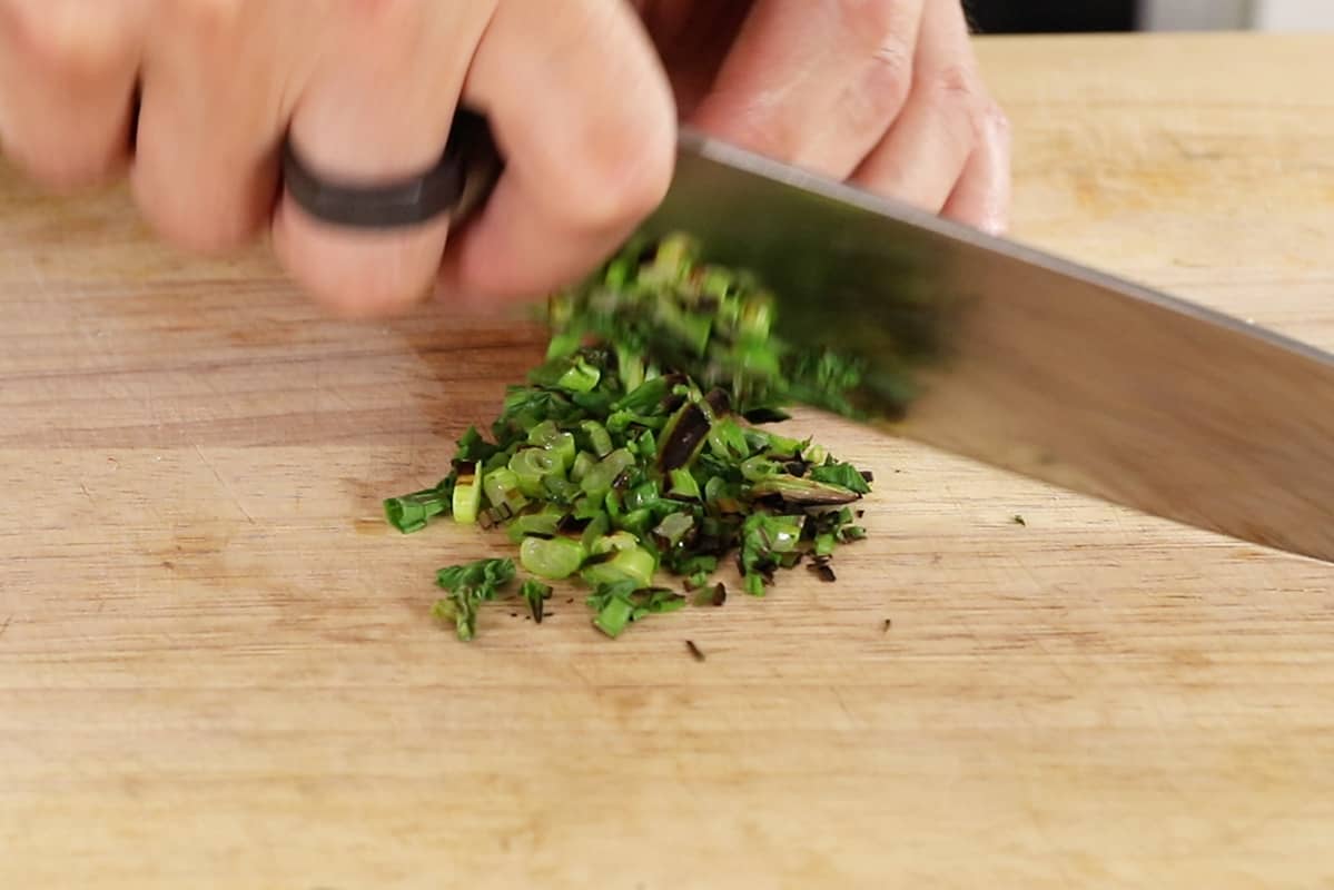 chopping charred scallions on wooden cutting board
