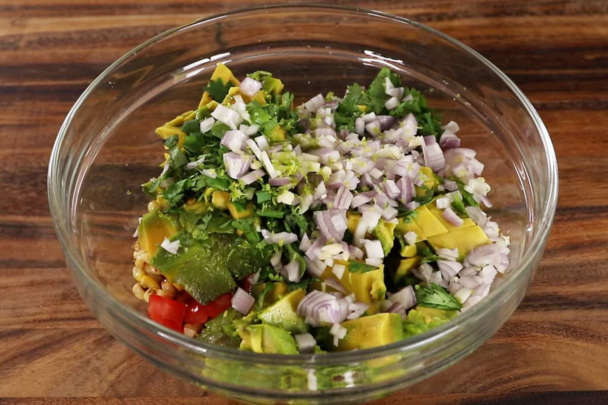 mixing avocado corn salad ingredients in glass bowl