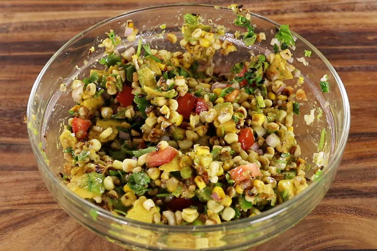 mixing avocado corn salad ingredients in glass bowl