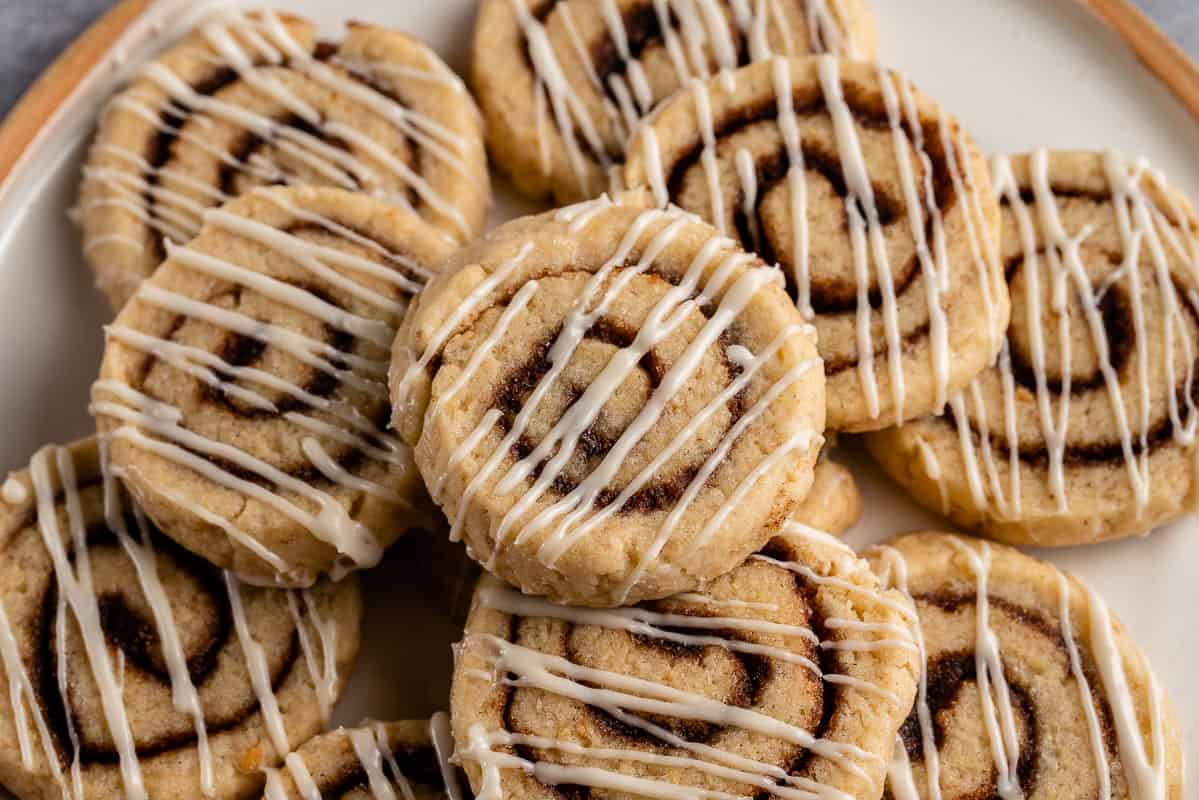 close up photo of cream cheese frosted cinnamon roll cookies stacked on plate