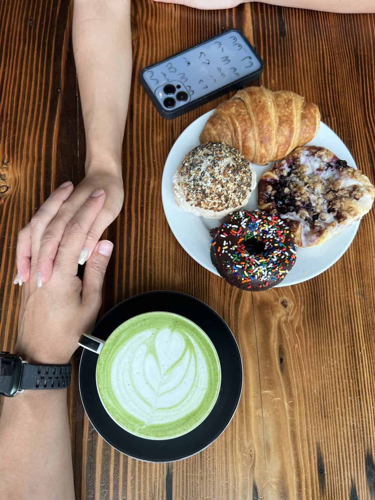 holding hands next to vegan matcha latte and pastries at Timeless Coffee in Oakland, CA