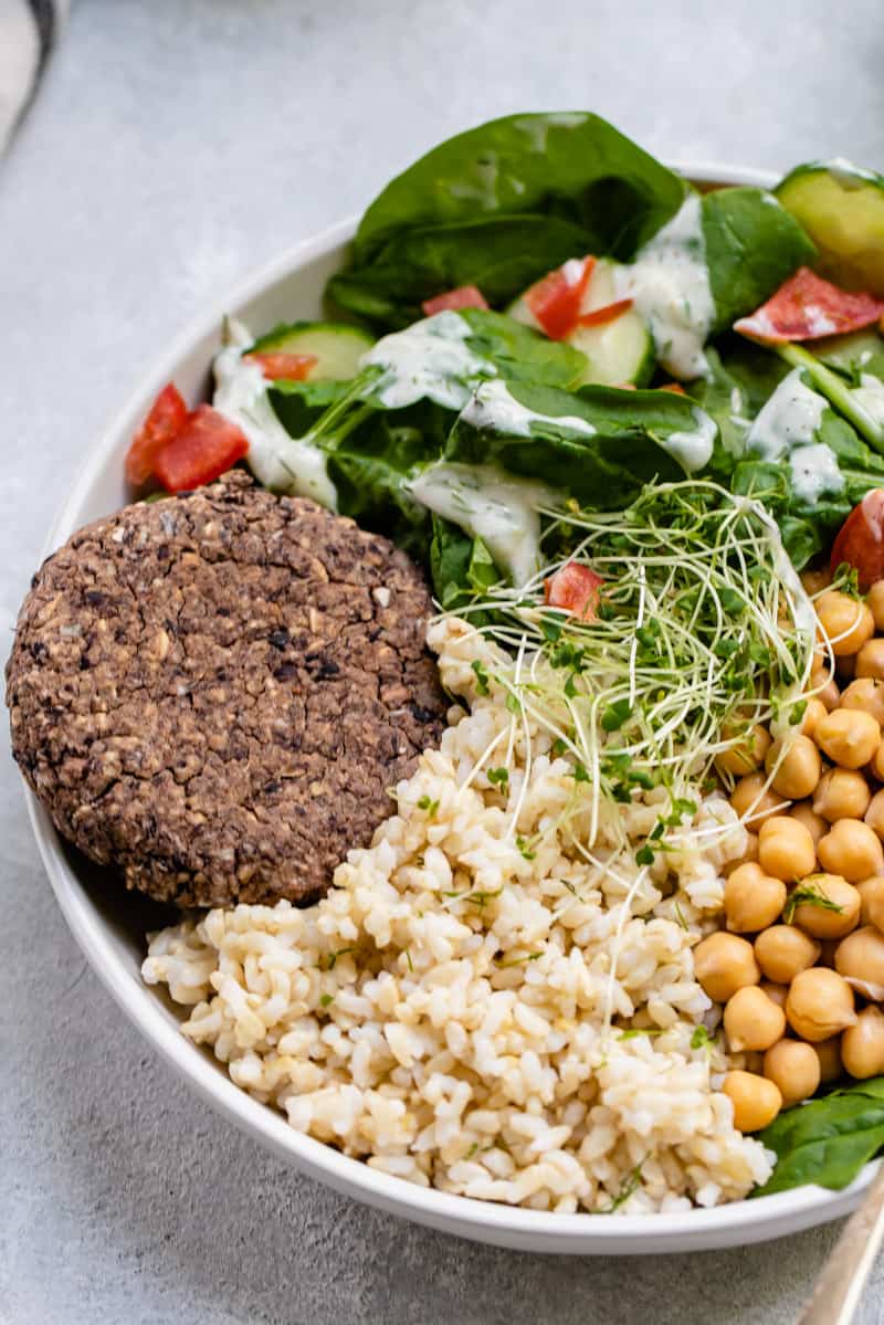 black bean burger in bowl with salad, rice, chickpeas and sprouts